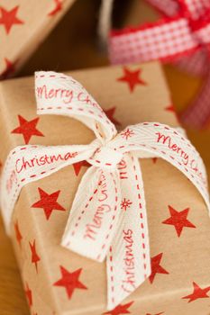 Close up vertical shot of several present boxes in kraft paper decorated with ribbons and red star pattern, on wooden surface