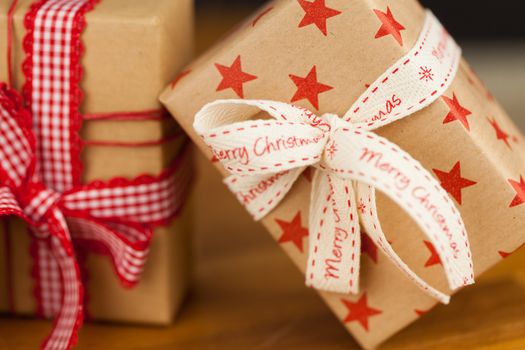 Close up vertical shot of several present boxes in kraft paper decorated with ribbons and red star pattern, on wooden surface