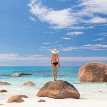 Woman wearing black bikini and beach hat, enjoying amazing view on Anse Lazio beach on Praslin Island, Seychelles. Summer vacations on picture perfect tropical beach concept.