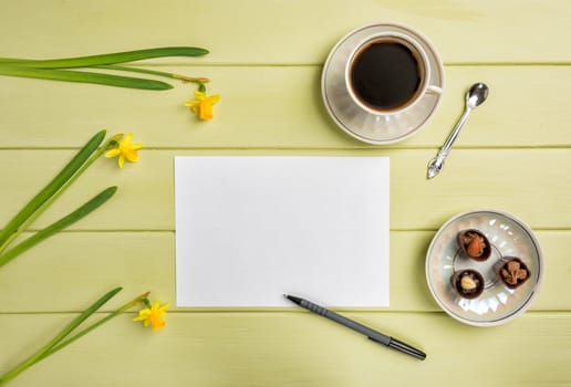 Paper, a pen, cup of black coffee and flowers on a wooden background. Top view. Copy space.