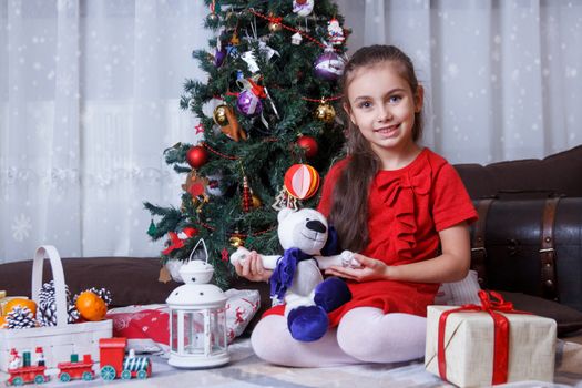 Smiling girl with plush bear under Christmas tree