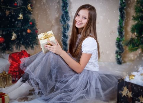 Smiling girl sitting with gift box under Christmas tree