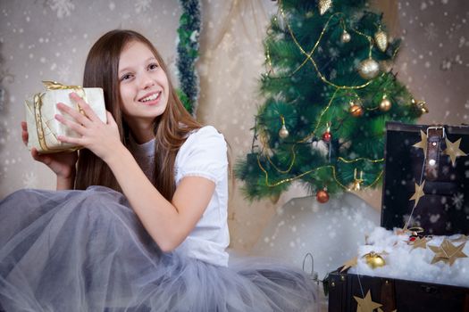 Pretty girl holding gift box under Christmas tree