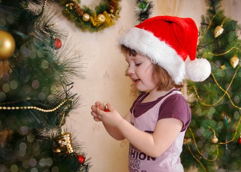 Cute girl decorating Christmas tree in red cap