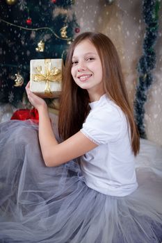 Pretty girl holding gift box under Christmas tree