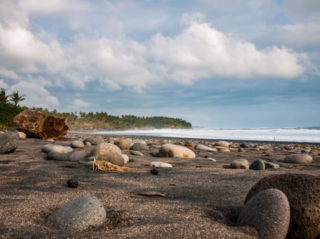 Pebbles on a beach with a tree trunk and cloudy sky