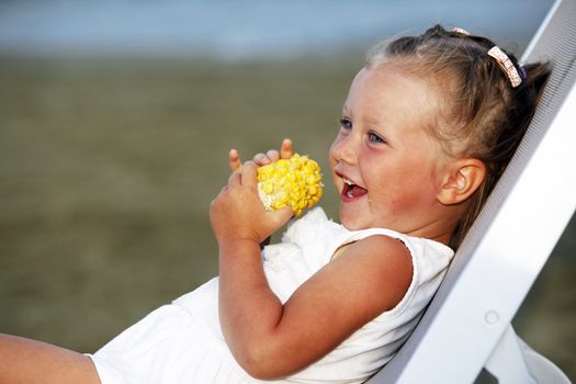 Little funny girl eating a boiled corn