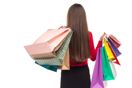 Long-haired young woman wearing red blouse and black skirt from her back holds colourful shopping paper bags