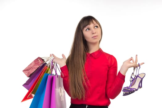 Young long-haired woman holds her purchases, many colorful paper bags, packages, and shoes in her hands after shopping