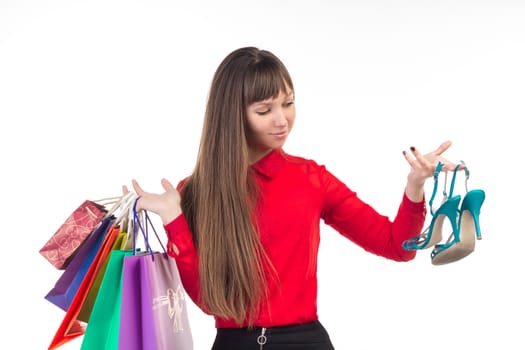 Young long-haired woman holds her purchases, many colorful paper bags, packages, and shoes in her hands after shopping