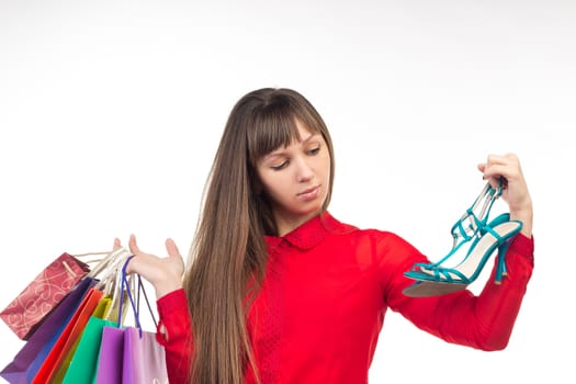 Young long-haired woman holds her purchases, many colorful paper bags, packages, and shoes in her hands after shopping