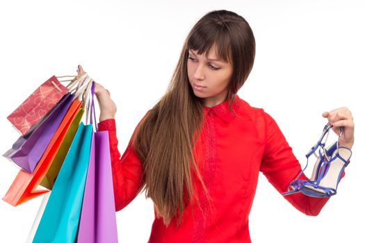 Young long-haired woman holds her purchases, many colorful paper bags, packages, and shoes in her hands after shopping