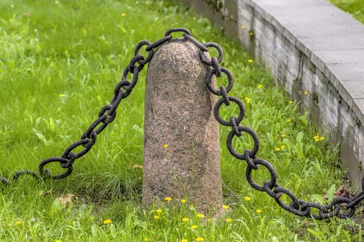granite pedestal with a chain on a background of green grass old guard
