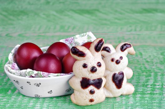 Easter cookies bunnies and colored eggs in the bowl, on the old green boards. Selective focus, space for text.