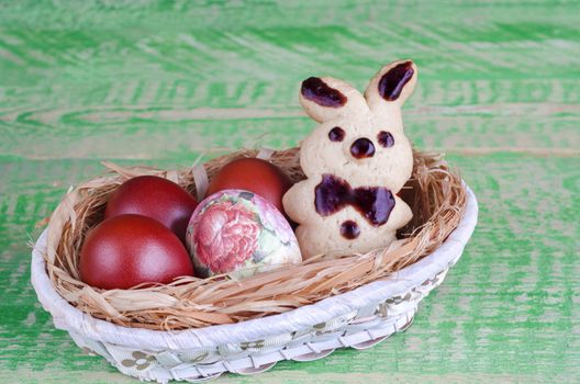 Easter cookies bunnies, decoupage and painted eggs in a basket, on the old green boards. Selective focus, space for text.