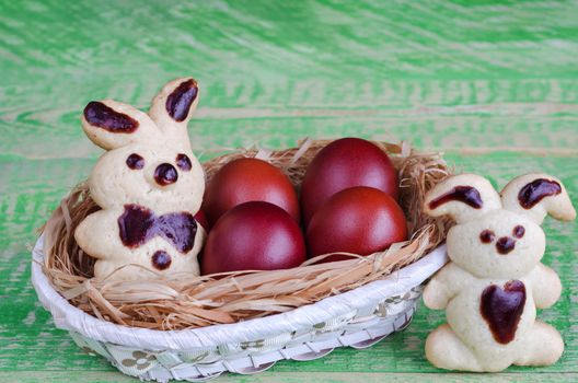 Easter cookies bunnies and colored eggs in a basket, on the old green boards. Selective focus, space for text.
