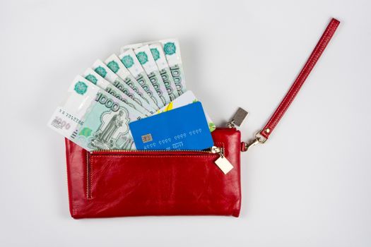 Red purse from which stick out money and credit cards on a white background