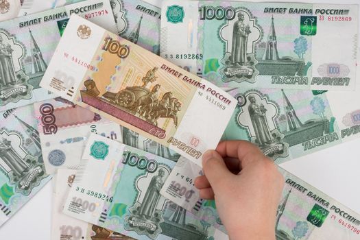 Children's hand takes the denomination from the pile of randomly scattered Russian banknotes of different denomination