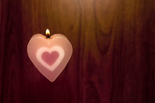 Candles shape heart pink color were lit on wood background. Love symbol for Valentine's day concept.