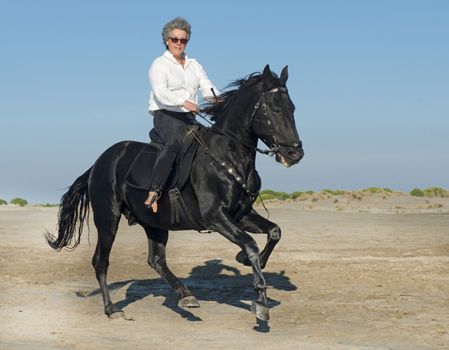 horse woman galloping with her black stallion on the beach