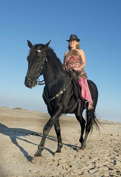 horse woman and her stallion riding on the beach