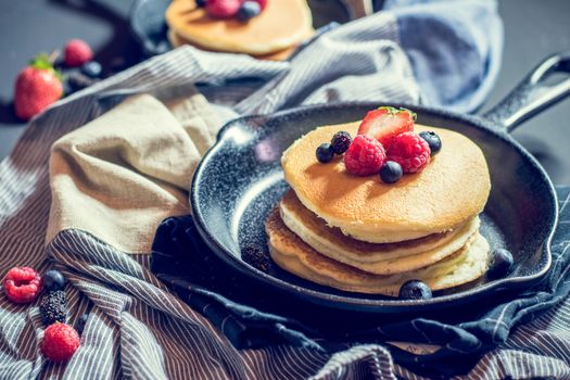 Home made pancakes with berries on metal frying pan decorated with berries (blueberries, raspberries and blackberries). Top View.