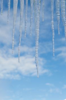 Closeup of a group of icicles against a blue sky with clouds