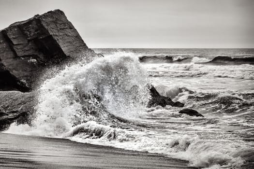 Black and white image of a large wave crashing on the shore.