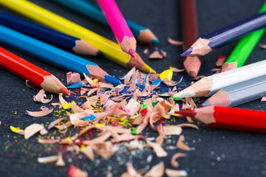 Colourful pencils with knot of wooden shavings on black surface background