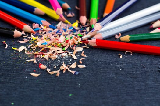 Colourful pencils with knot of wooden shavings on black surface background