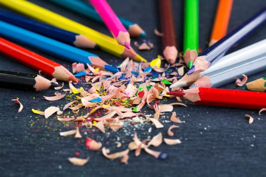 Colourful pencils with knot of wooden shavings on black surface background