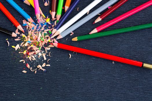 Colourful pencils with knot of wooden shavings on black surface background