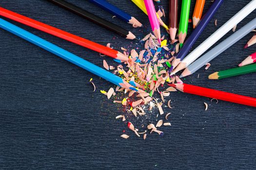 Colourful pencils with knot of wooden shavings on black surface background
