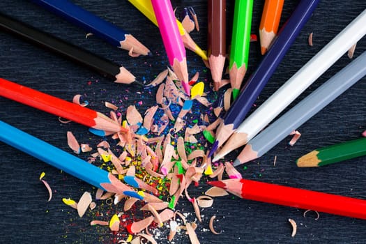 Colourful pencils with knot of wooden shavings on black surface background