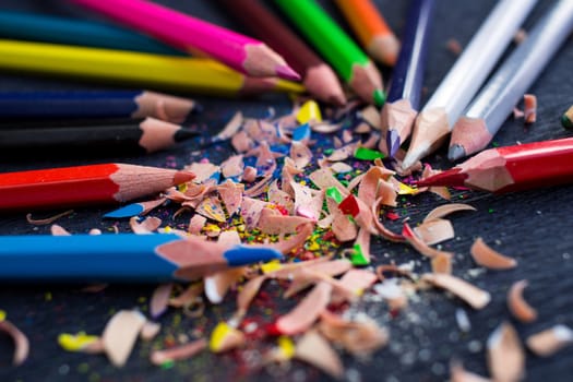 Colourful pencils with knot of wooden shavings on black surface background