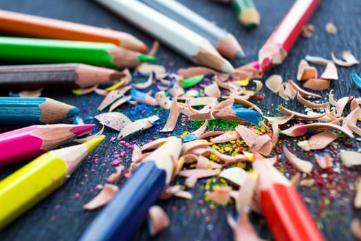 Colourful pencils with knot of wooden shavings on black surface background