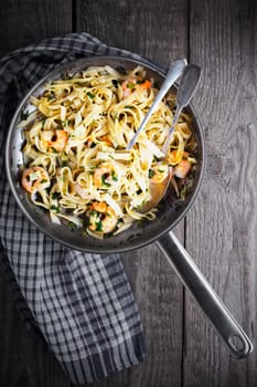 Tagliatelle with shrimps on the pan served on a wooden surface