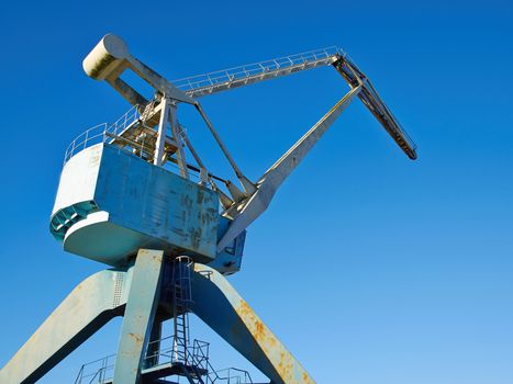 Traditional industrial metal port crane with clear blue sky background
