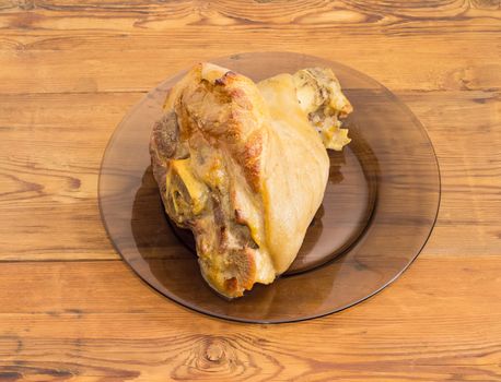 Baked ham hock on a glass dish on a surface of old wooden planks
