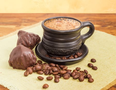 Freshly brewed coffee latte in a black ceramic cup, roasted coffee beans and two chocolate truffles on a napkin on a wooden surface
