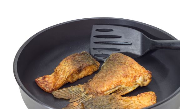 Fragment of an aluminium cast frying pan with ceramic non-stick coating with fried tail portion and other slices of carp and plastic spatula on a light background
