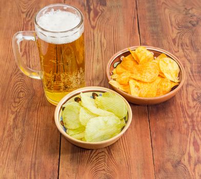 Glass tankard with lager beer, potato chip flavored paprika and wasabi in two different ceramic bowls on an old wooden planks
