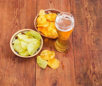 Top view of the beer glassware with the lager beer, two different kinds of the potato chip flavored paprika and wasabi in ceramic bowls on an old wooden table
