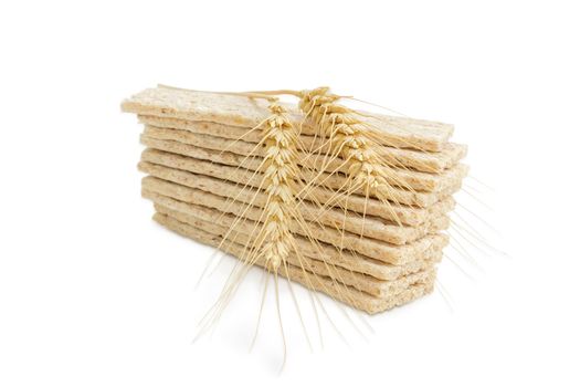 Pile of the dietary wheat wholegrain crispbread with adding a buckwheat and a barley and two wheat spikes on her closeup on a light background
