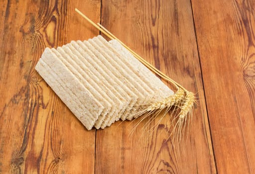 Dietary wheat wholegrain crispbread with adding a buckwheat and a barley and two wheat spikes on a surface of an old wooden planks
