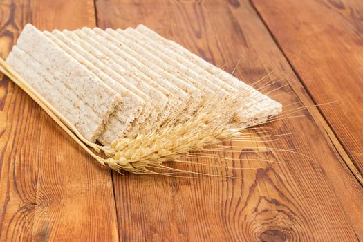 Several dietary wheat wholegrain crispbread with adding a buckwheat and a barley and two wheat spikes closeup on a surface of an old wooden planks
