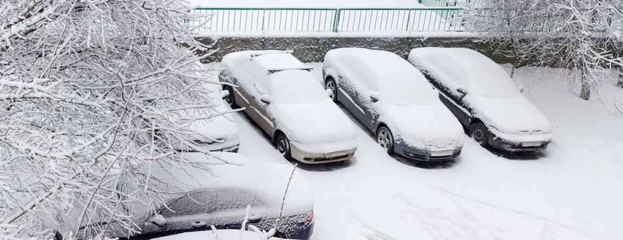 Top view through the trees branches of the parking lot with cars covered with snow in a residential area during heavy snowfall
