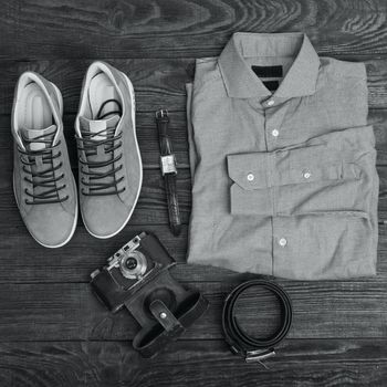 Flat lay of modern men's clothing on a brown wooden background. Top view of hipster clothes and accessories. Black and white photography