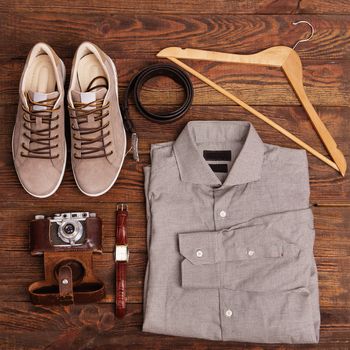 Flat lay of modern men's clothing on a brown wooden background. Top view of hipster clothes and accessories