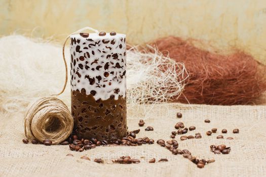 Beautiful Decorative Handmade candle with coffee beans on old sackcloth background. Candlelight.